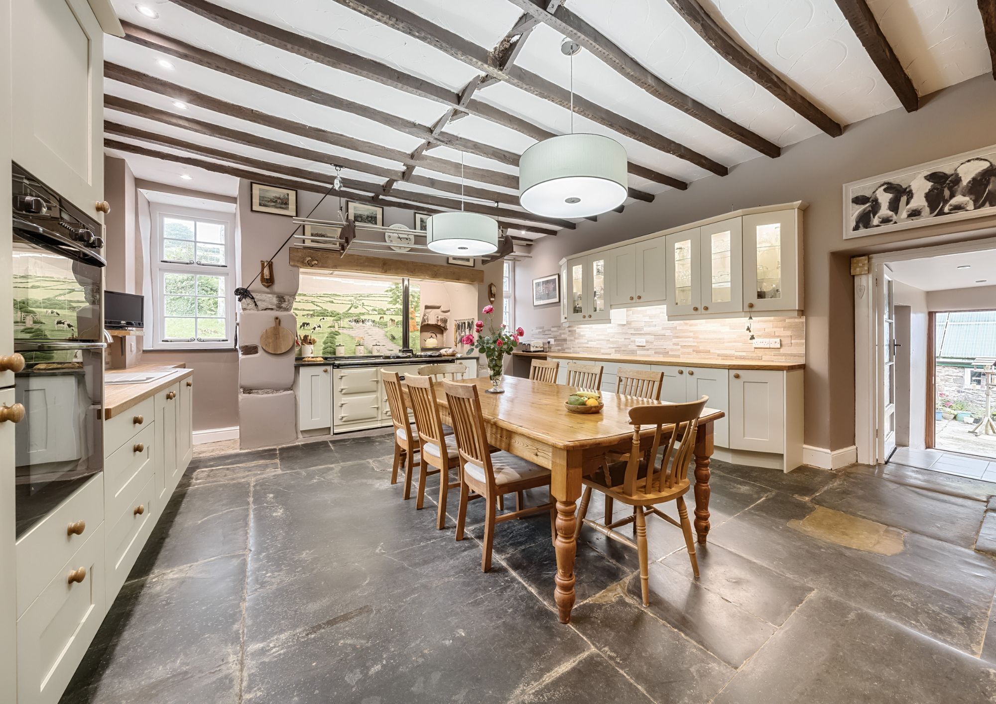 A country style kitchen in a period farmhouse with ceiling beams a large dining table and an Aga.