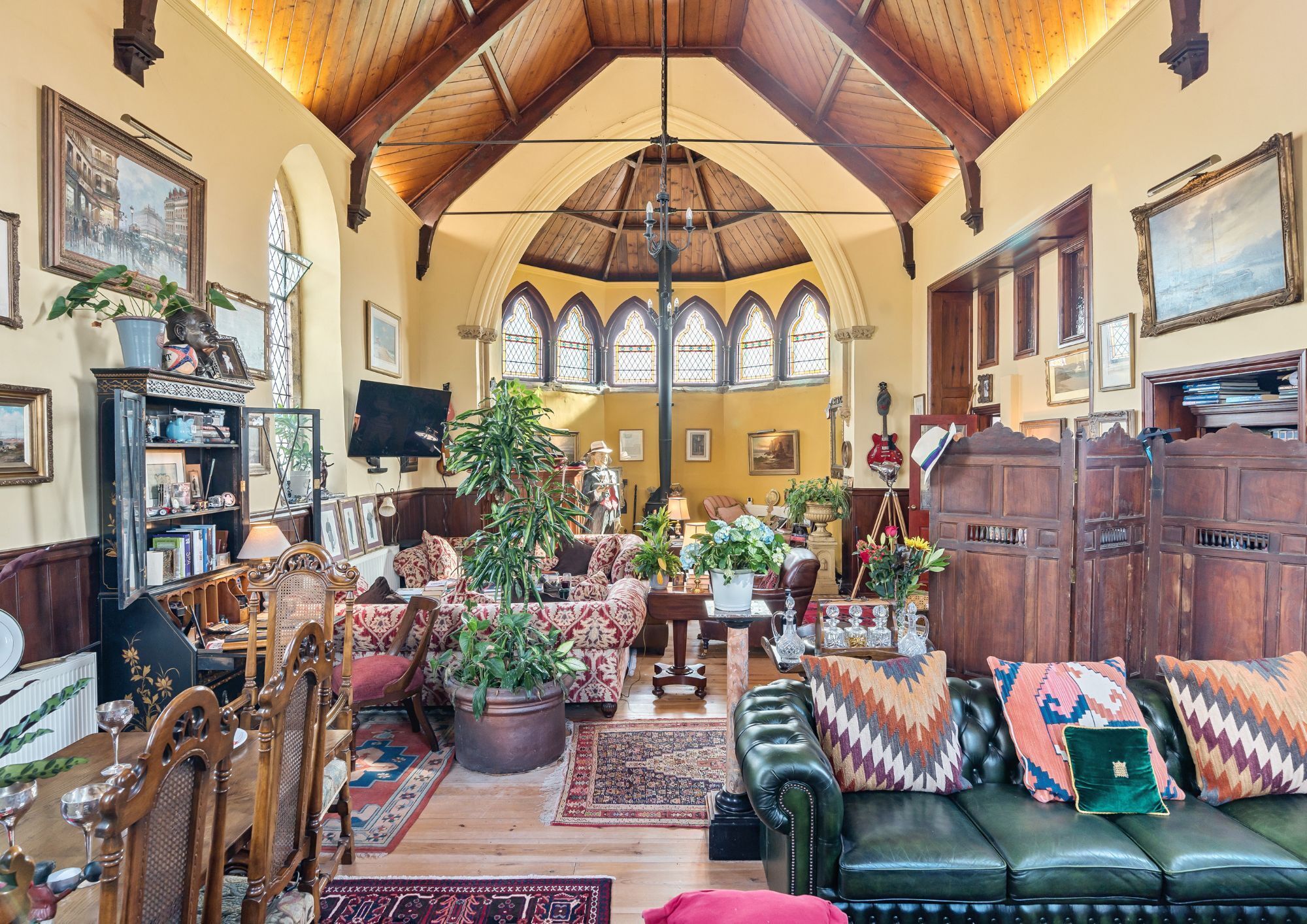 Living area of the converted chapel, with a high vaulted ceiling and original features such as stained glass windows and wooden beams.