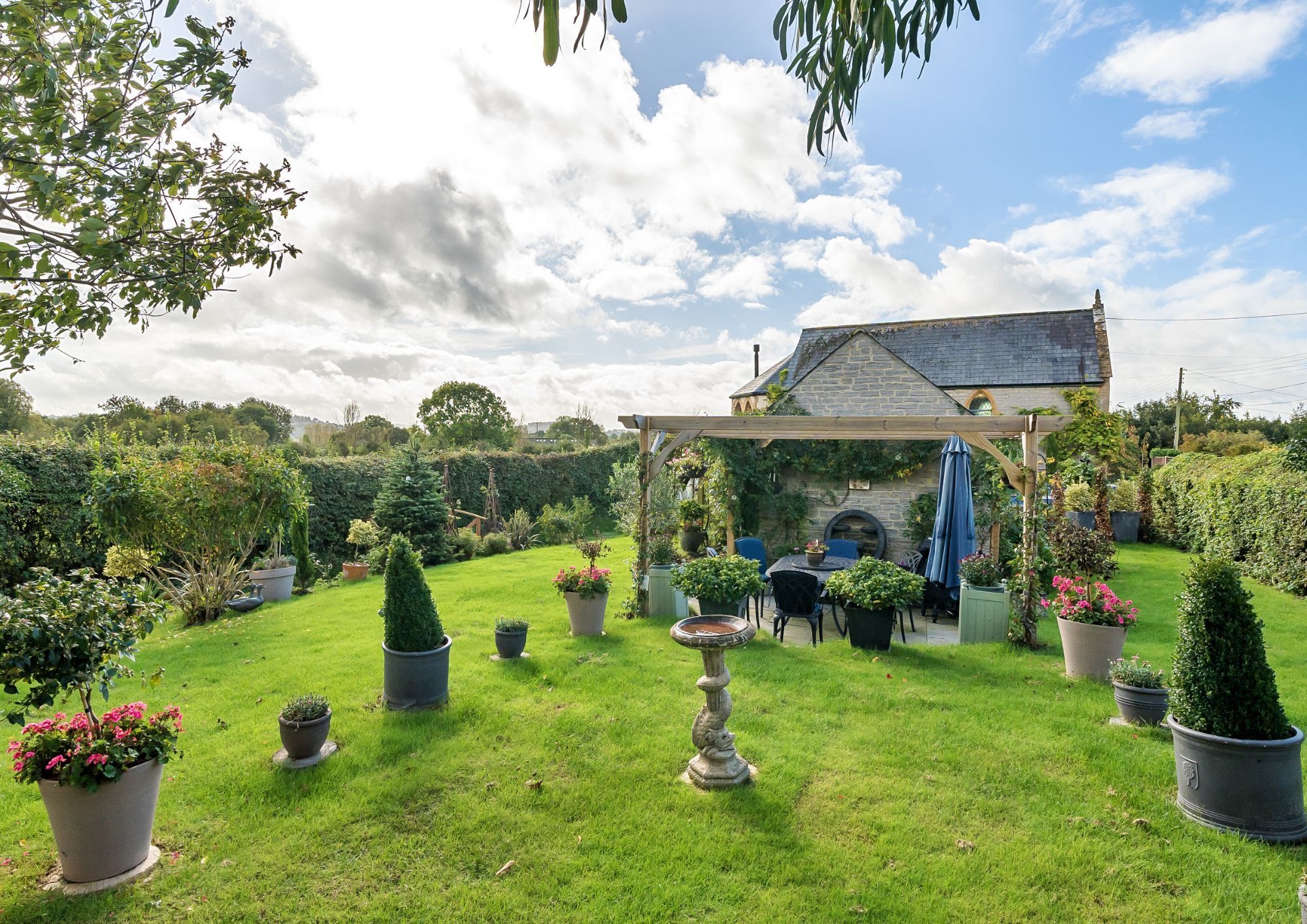 Garden of the converted chapel including a lawn, patio and a variety of shrubs.