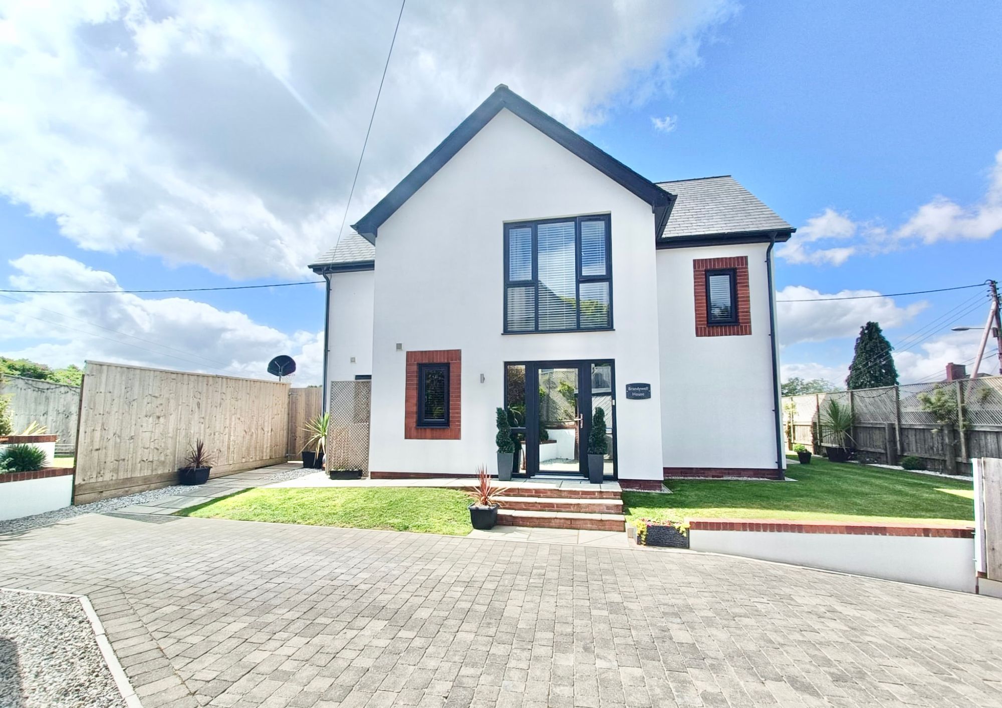 A white rendered, modern detached house with front garden and driveway.