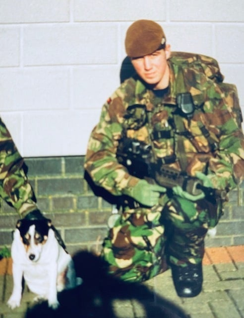 Photo of Stuart Benson crouched in military gear with a rifle