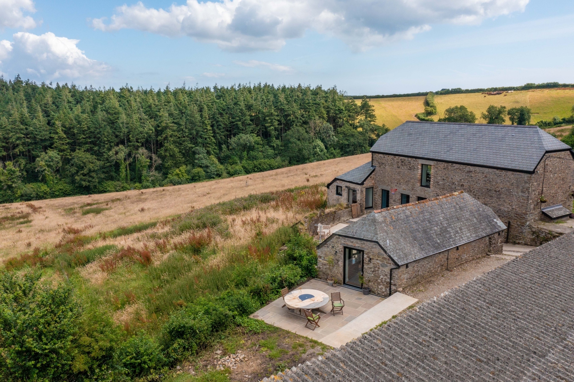 A stone house with a garden, backed by woodland