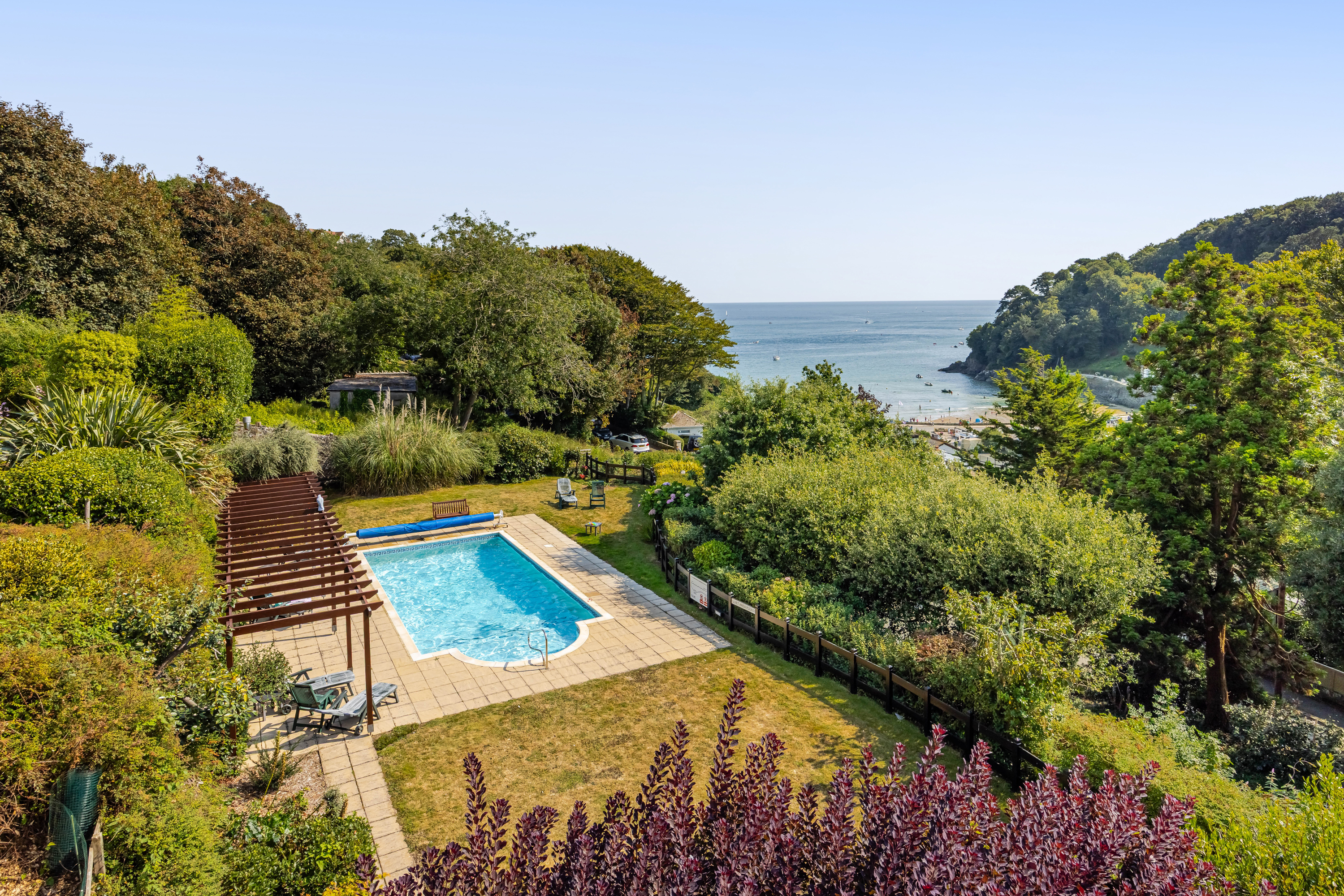 Shot of swimming pool surrounded by greenery and North Sands Beach in Salcombe in the background