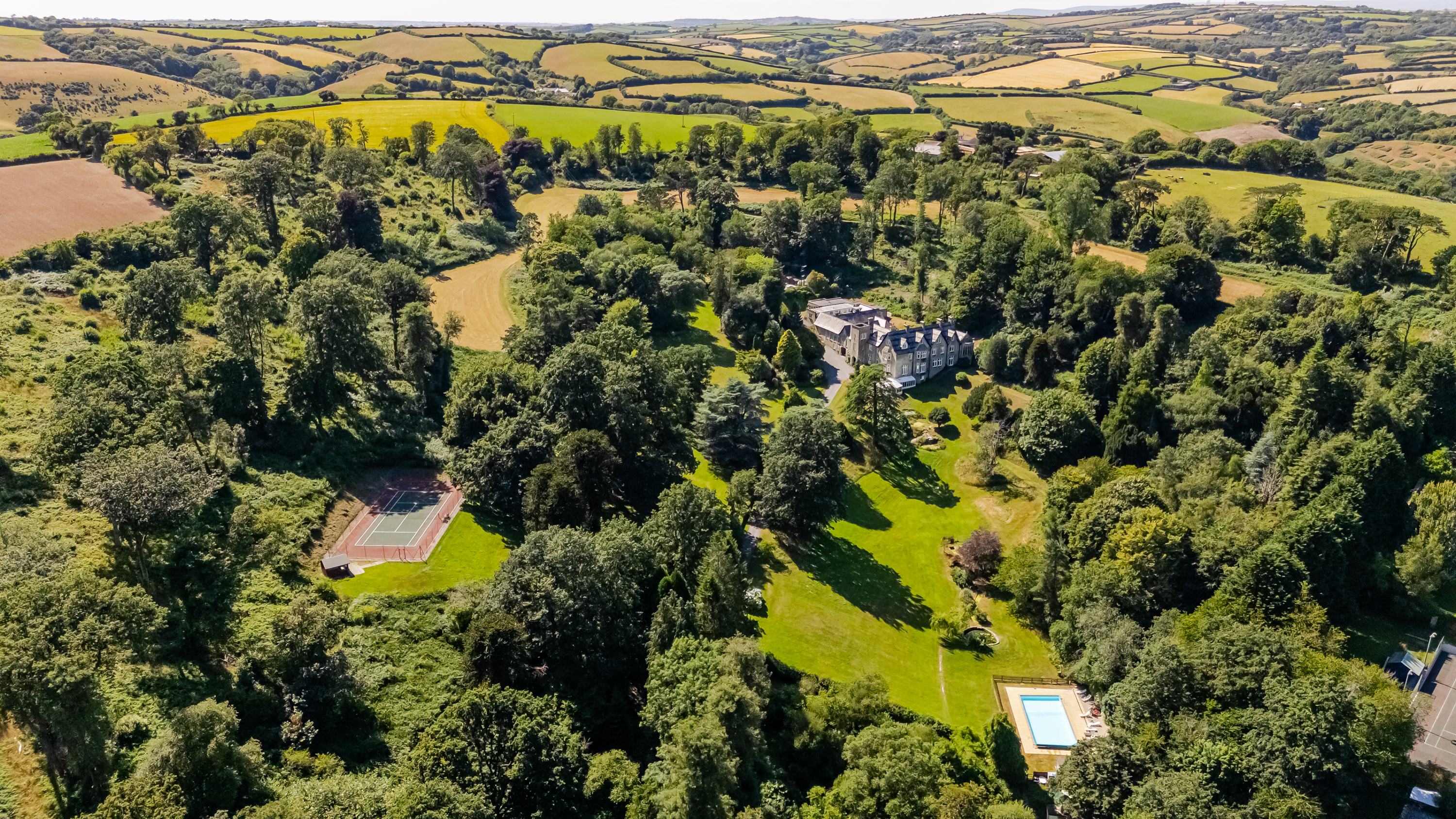 Aerial view of large estate surrounded by fields and trees with a swimming pool and tennis courts