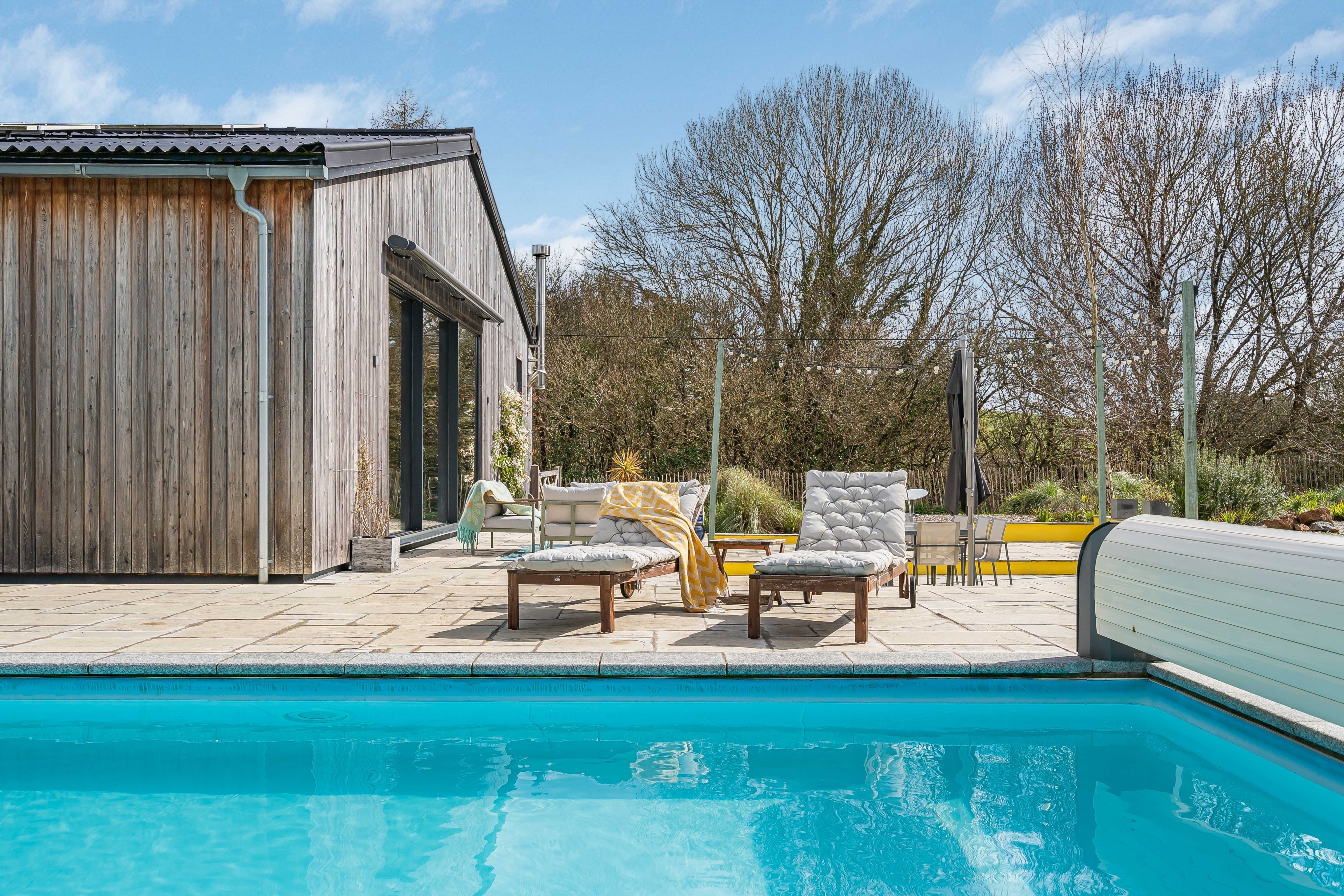 wooden cladded home with swimming pool and sun loungers in foreground 